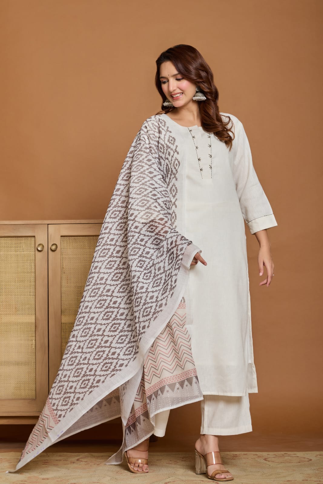 Woman wearing a white kurta with a patterned dupatta against a brown background