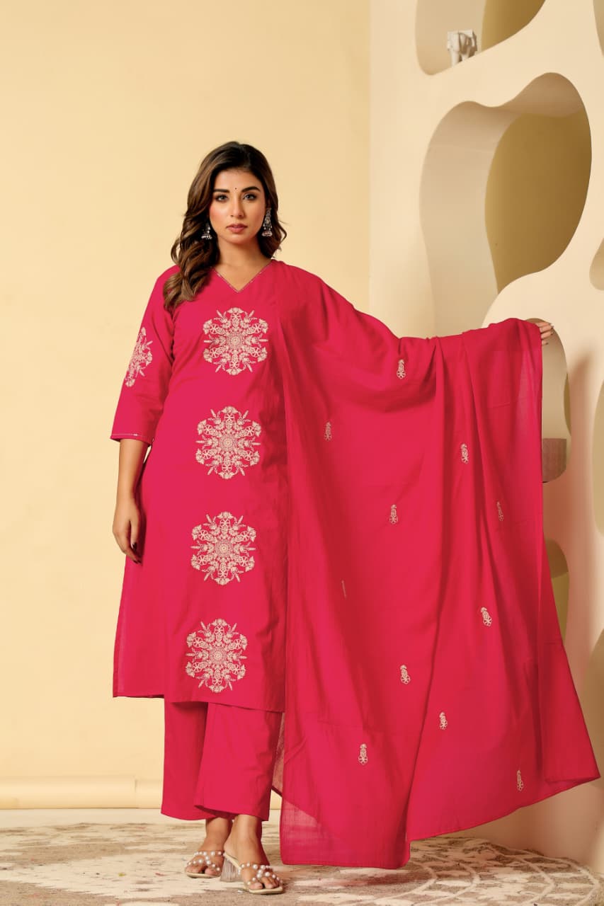 Woman wearing a pink traditional outfit with white embroidery against a beige wall.
